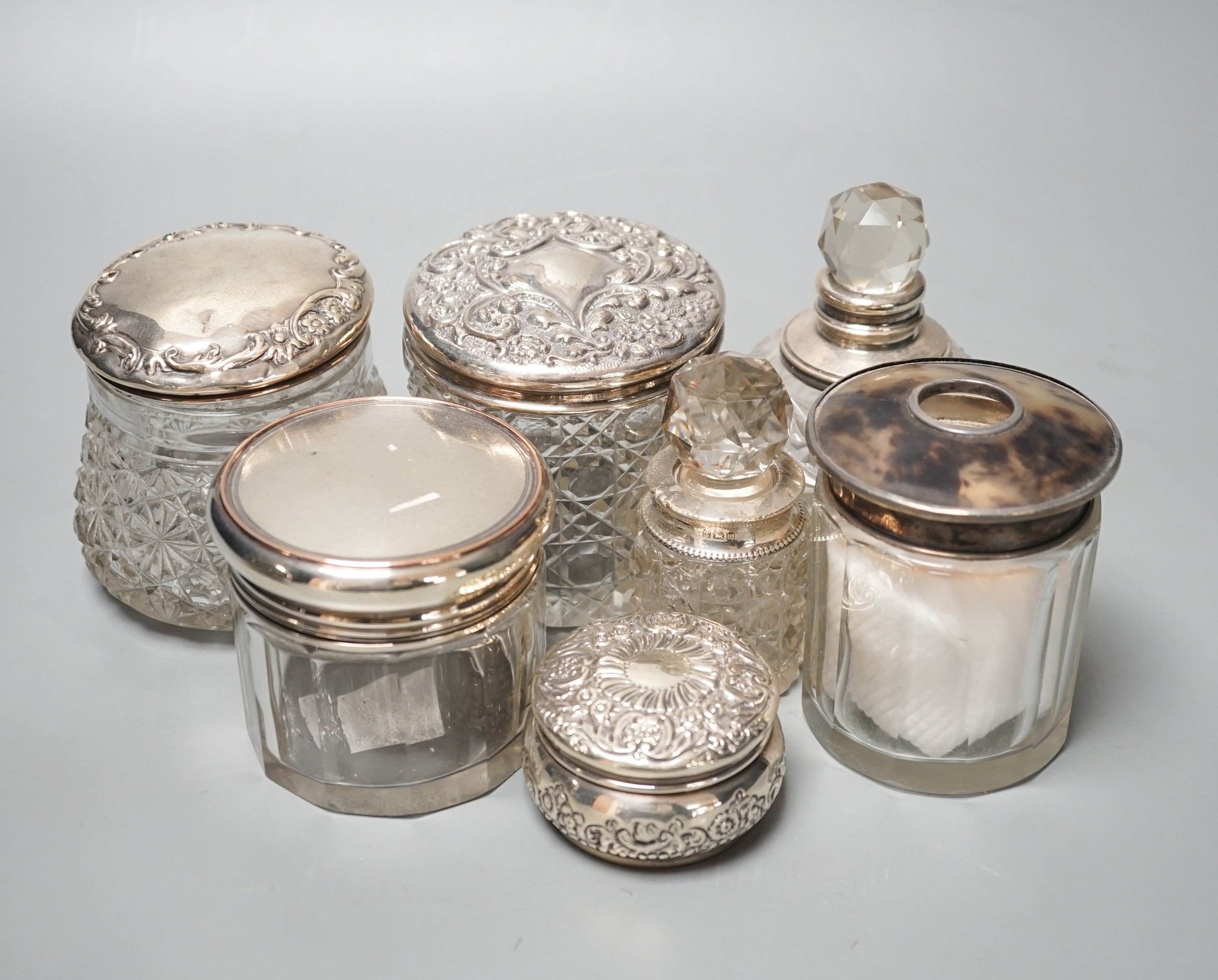 A circular embossed silver box and six silver mounted glass toilet bottles.
